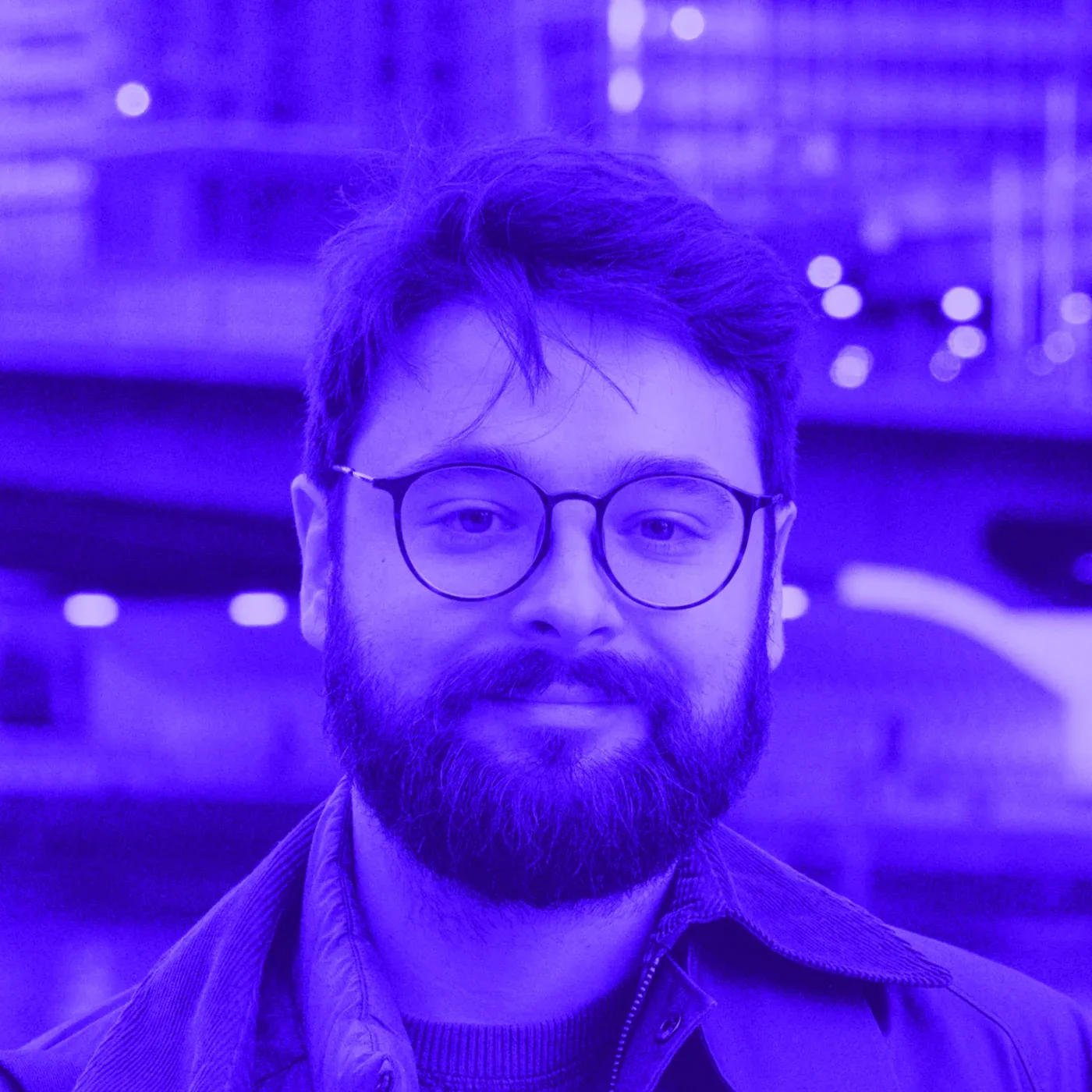 Portrait of Joe Van Hove, a bearded man in round glasses, in a blue-tinted photo.